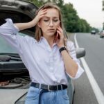 Young,Woman,Standing,Near,Broken,Down,Car,With,Popped,Up